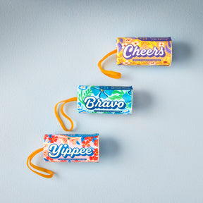 Colorful seed confetti poppers labeled "Cheers," "Bravo," and "Yippee" arranged on a light blue background.