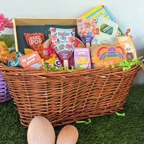 Woven Easter basket filled with seed packets, candy, and gardening items, surrounded by decorative grass and wooden eggs.