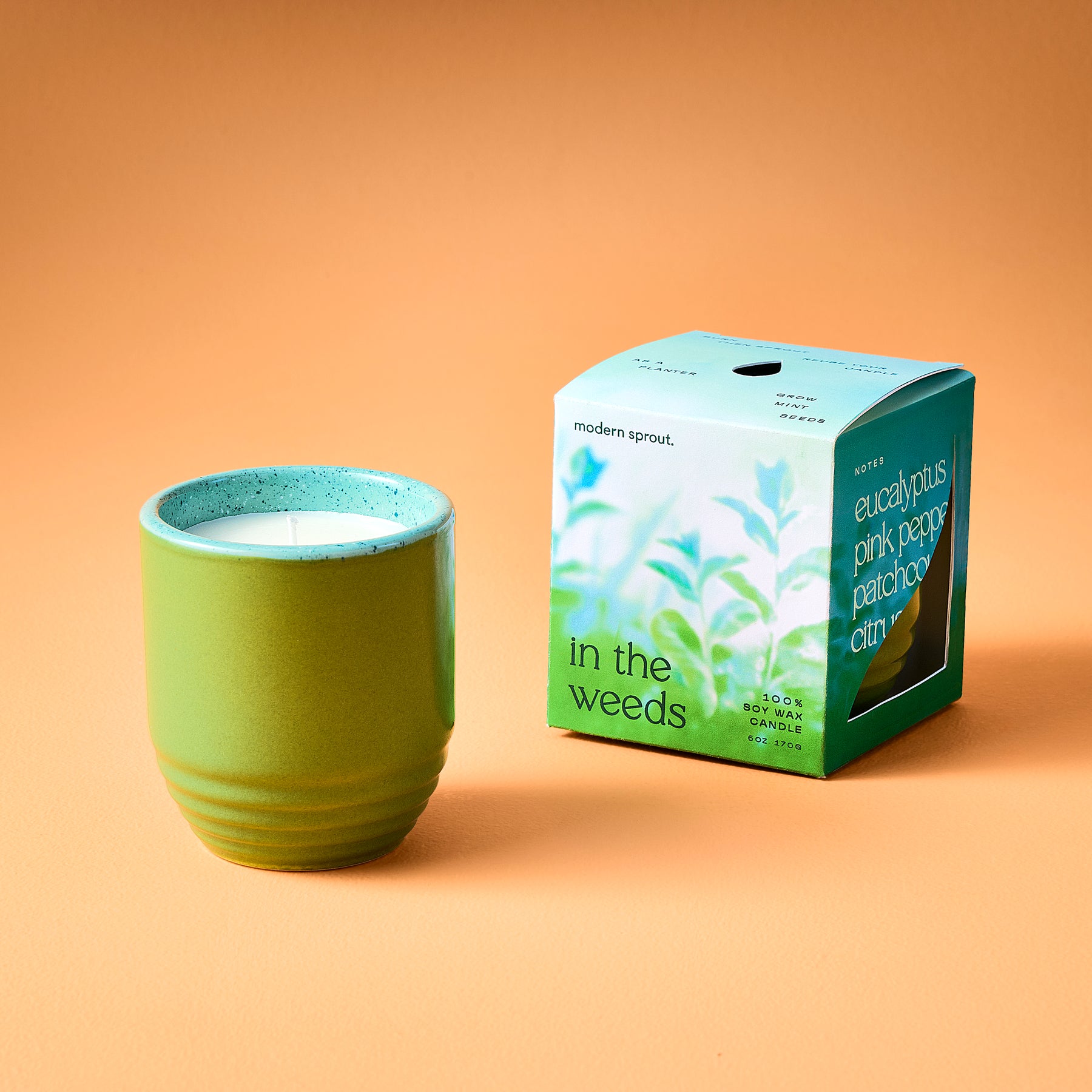 Green ceramic candle planter with a white candle inside, next to a colorful box labeled "eucalyptus pink pepper patchouli citrus.