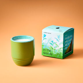 Green ceramic candle planter with a white candle inside, next to a colorful box labeled "eucalyptus pink pepper patchouli citrus.