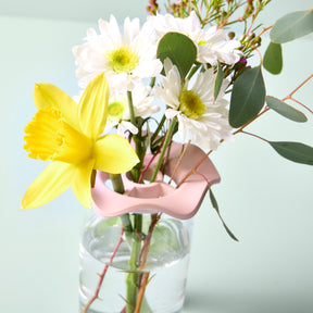 Two Botanical Keepers in use, holding fresh flowers, including a yellow daffodil and white daisies, in a clear vase.