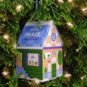Colorful lavender grow kit ornament shaped like a house, hanging on a green tree branch, promoting indoor gardening.