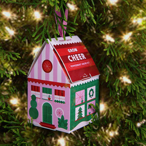 Colorful peppermint grow kit shaped like a house ornament, hanging on a Christmas tree with twinkling lights.