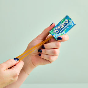 A hand holds a colorful seed confetti popper, pulling back the elastic band ready to launch seeds.