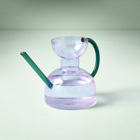 Elegant glass watering can with a purple body and green handle, designed for stylish indoor plant care.