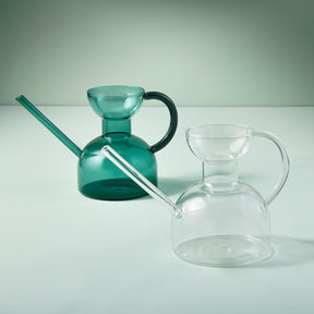 Two elegant glass watering cans in green and clear, featuring unique shapes and long spouts for precise watering.