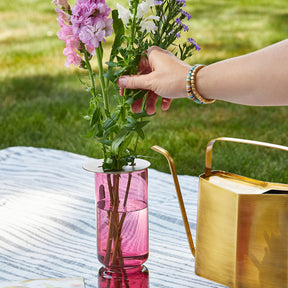 Brass flower frog placed in a pink vase, supporting fresh flowers while a hand adjusts the arrangement outdoors.