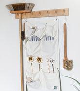 Hanging organizer apron with multiple pockets, tools, and a broom, mounted on a wall for easy access and storage.