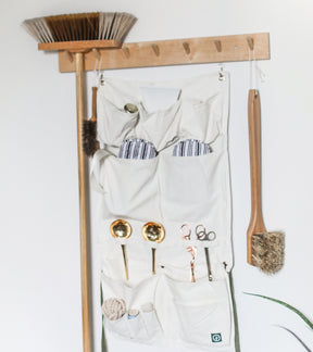 Hanging organizer apron with multiple pockets, tools, and a broom, mounted on a wall for easy access and storage.