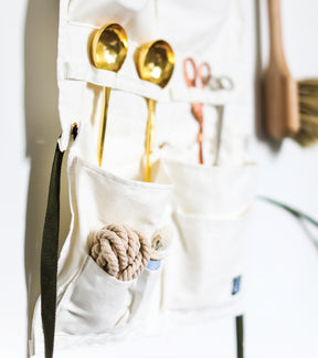 Hanging organizer and apron featuring multiple pockets, holding kitchen utensils and tools in a clean, minimalist design.
