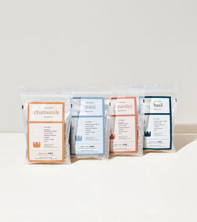 Four packets of herb seeds for chamomile, mint, parsley, and basil, each labeled with planting instructions and details.