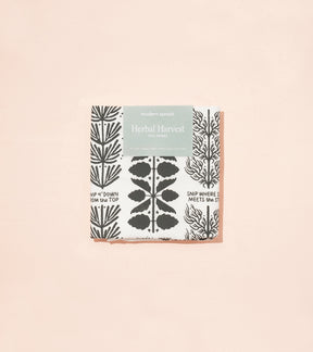 Herbal Harvest tea towel featuring botanical illustrations in black and white with a peach border, packaged attractively.